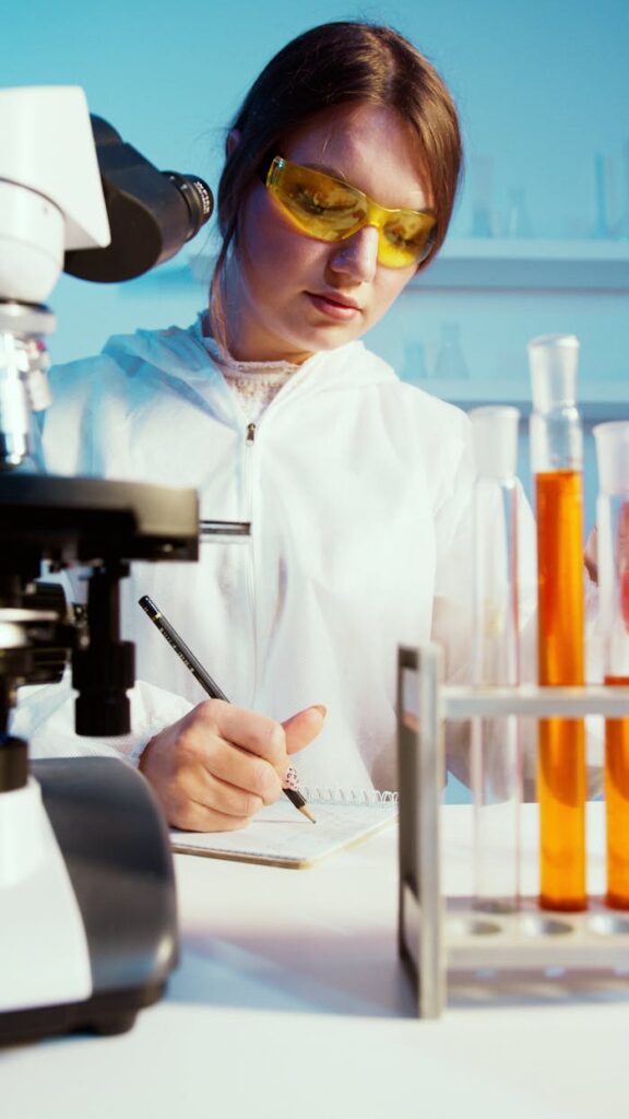 Quizzes A female scientist writes notes in a lab among test tubes and a microscope.