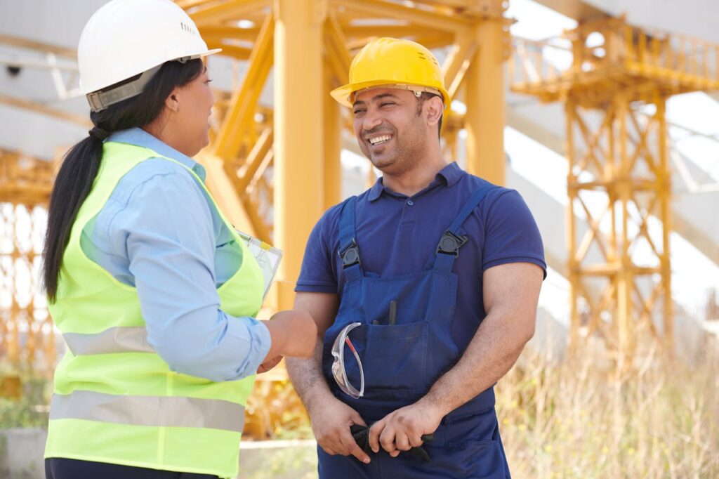 Quizzes Two construction workers in hardhats smiling and talking on a sunny day at a site.